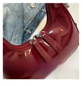 Detailed close-up of burgundy patent leather texture and dual zipper hardware on crescent bag