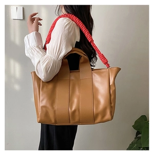 Detail view of large tote bag featuring unique red ruffled shoulder strap and tan leather