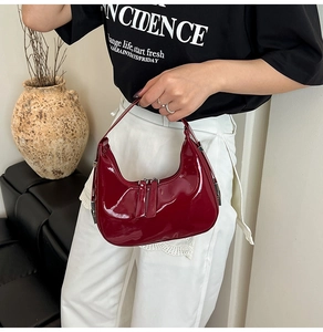 Detailed macro view of burgundy patent leather finish and dual zippers on hobo bag