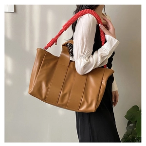 Borsa tote in pelle marrone con tracolla a treccia rossa indossata da una modella