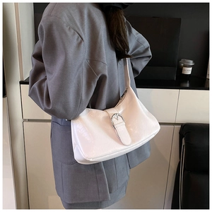 Close-up of white Hobo shoulder bag with silver buckle worn with a gray suit