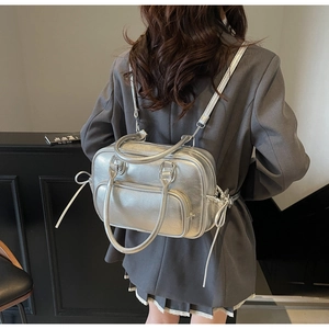 Silver metallic backpack with bow detail worn by a model in a modern grey suit
