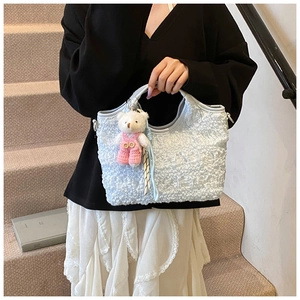 Détail d'un sac à main bleu clair à texture bulle avec un pendentif ours en peluche
