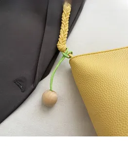 Detail of yellow pebble leather bucket bag with woven handle and wooden bead charm