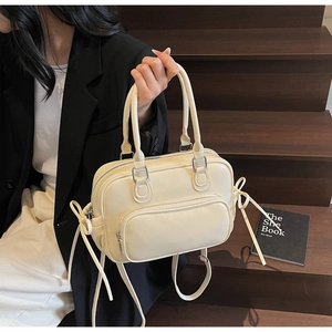 Detail of beige leather Boston bag featuring side ribbon bows and a front zipper pocket