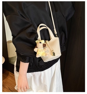 Detail of cream lychee textured bucket bag with metal lock and cute puppy charm