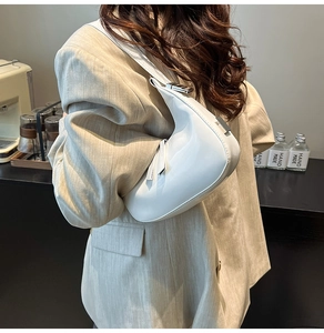 Detail of white patent leather crescent bag with silver buckle worn on shoulder