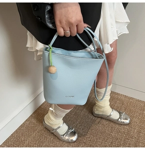 Detail of light blue bucket bag with wood bead charm and lychee texture leather