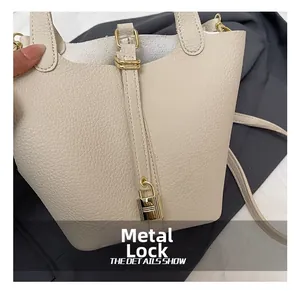 Close-up of off-white lychee grain leather bucket bag with golden padlock hardware detail