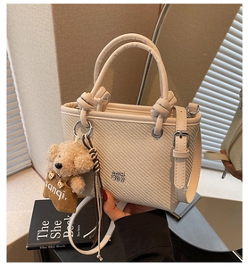Detail of cream woven bucket bag featuring teddy bear charm and metallic logo on the front