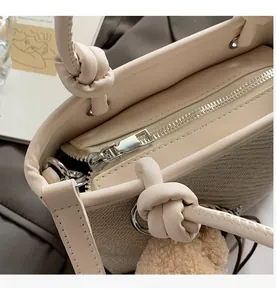 Close-up of smooth metal zipper and knotted handle on beige textured bucket bag
