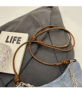 Detail of blue denim crescent bag featuring brown leather knotted strap and silver hardware