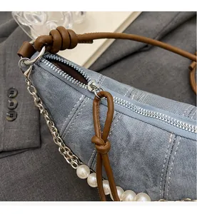 Close-up of a smooth silver zipper on a light blue denim half-moon bag with pearl chain