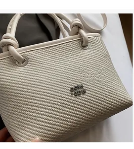Close-up of beige woven texture handbag with metal logo and cream handle detail