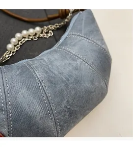 Close-up of light blue croissant bag with white stitching, pearl chain and woven strap
