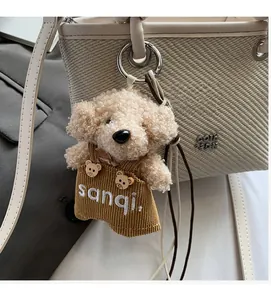 Detail of plush teddy dog charm with striped overalls attached to a woven handbag