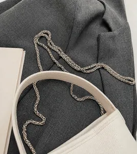 Detail van de witte bucket bag van lychee leer met zilveren metalen ketting op een blazer