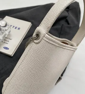 Detailopname van witte bucket bag van leer met lychee-patroon en zilveren metalen ketting