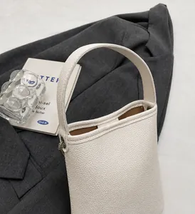 Detailopname van witte litchi-patroon lederen emmertas op een grijze blazer met rekwisieten