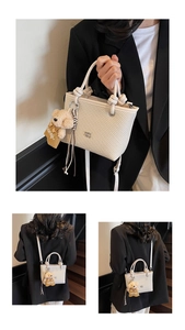 Detailed view of cream woven bucket bag with long strap and cute plush bear charm accessory