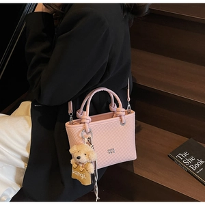 Pink bucket bag with textured leather, woven handles, and a cute teddy bear charm detail