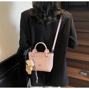 Detail of light pink bucket bag with knot handle, teddy bear charm, and striped scarf decor