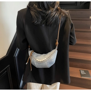 Dettaglio della borsa a mezzaluna in denim azzurro con catena di perle e tracolla marrone