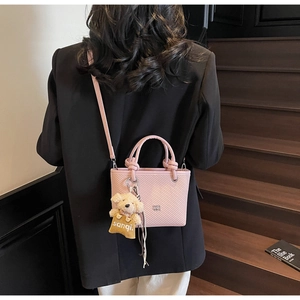 Detail of pink crossbody bucket bag with textured pattern and cute bear charm decoration