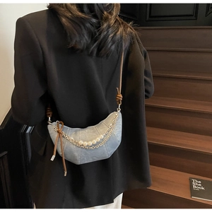Detail of light blue denim crescent bag featuring silver chains and pearl accents