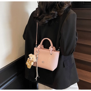 Close-up of pink textured crossbody bucket bag with bear charm on model in black suit