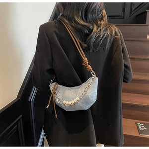 Détail d'un sac demi-lune en jean bleu clair avec perles blanches et chaîne argentée