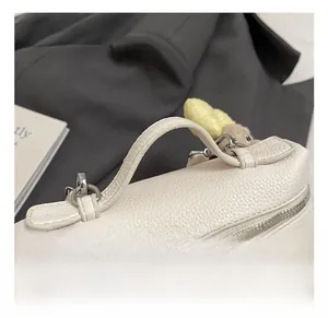 Close-up of white litchi pattern leather handbag featuring reinforced handle and metal zipper