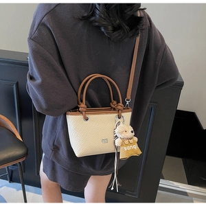 Detail of cream woven bucket bag with brown leather handle and cute teddy bear charm