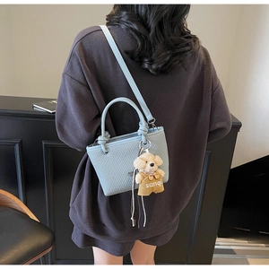 Detail of light blue bucket bag with woven texture and a cute teddy bear charm