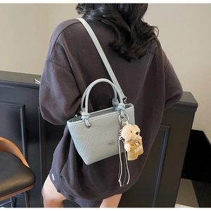 Detail of light blue textured crossbody bucket bag with cute plush bear charm on model
