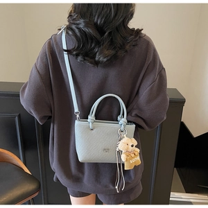 Detailed back view of a light blue woven bucket bag with a cute bear charm and shoulder strap
