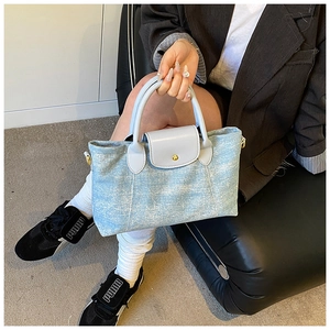Dettaglio borsa tote in denim azzurro con manici in pelle e fibbia con rivetto dorato