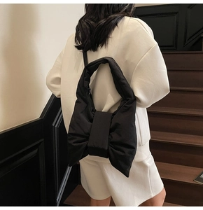 Rear view of a black bow-shaped puffer tote bag with a soft quilted texture on a model