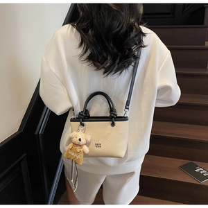 Detail of a beige woven bucket bag with black leather straps and a plush bear charm