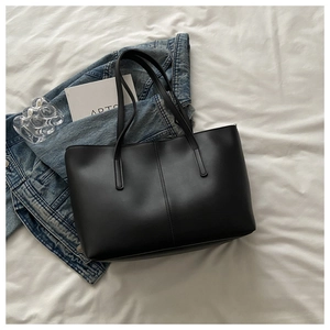 Detail of minimalist black leather tote bag with vertical stitching and long double handles