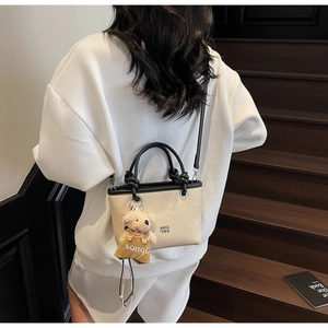 Straw texture bucket bag featuring black leather handles and a cute bear charm detail