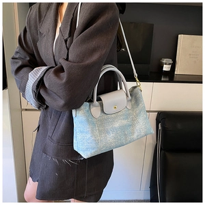 Dettaglio della borsa in denim azzurro con manici in pelle grigia e bottone in metallo oro