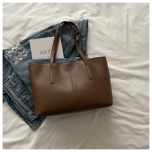 Detailed top view of a large brown tote bag on white sheets with a book and denim jacket