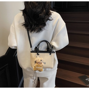 Top view of beige straw bucket bag with leather handles and cute bear charm detail