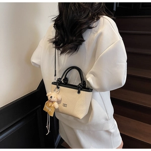 Detail of beige woven mini tote bag with black round handle and small bear charm