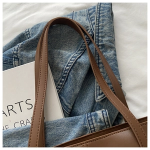 Detailed close-up of brown leather tote bag straps and fine stitching on white fabric