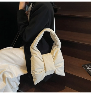 Detail of a creamy bow-shaped tote bag in quilted fabric held by a model in casual attire