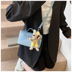 Detail of light blue lychee texture box bag featuring a plush puppy charm worn crossbody