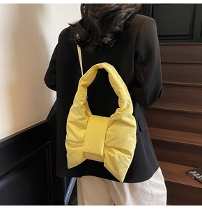 Detail of a bright yellow puffer tote bag with a large bow design worn by a model