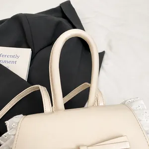 Detail of a beige ballet-style handbag featuring thick round handles and lace embroidery